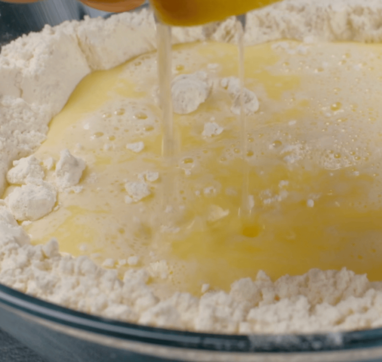 Wet ingredient mixture being poured into bowl with dry ingredient mixture of easy dinner rolls. 