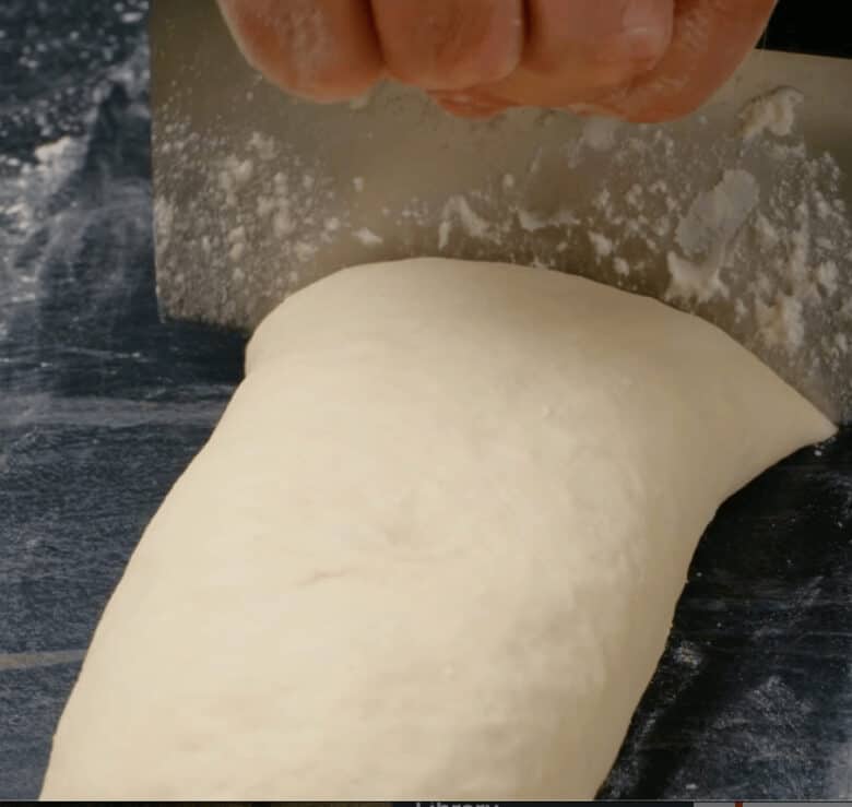 Easy dinner roll dough rolled into a log and being cut.