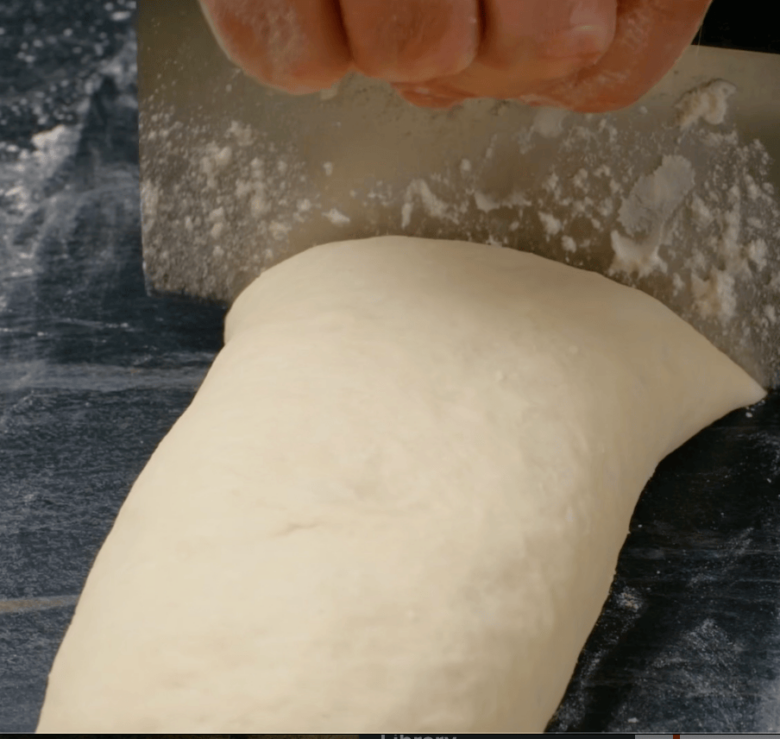 Easy dinner roll dough rolled into a log and being cut.