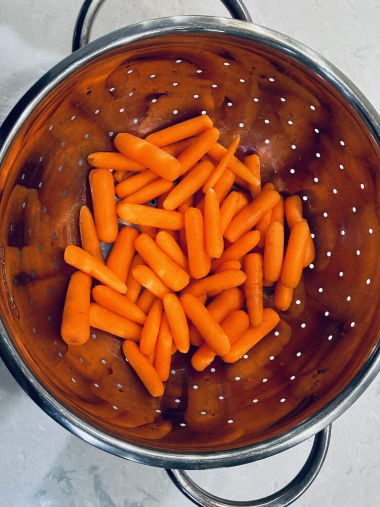 Baby carrots in a colander on a counter.