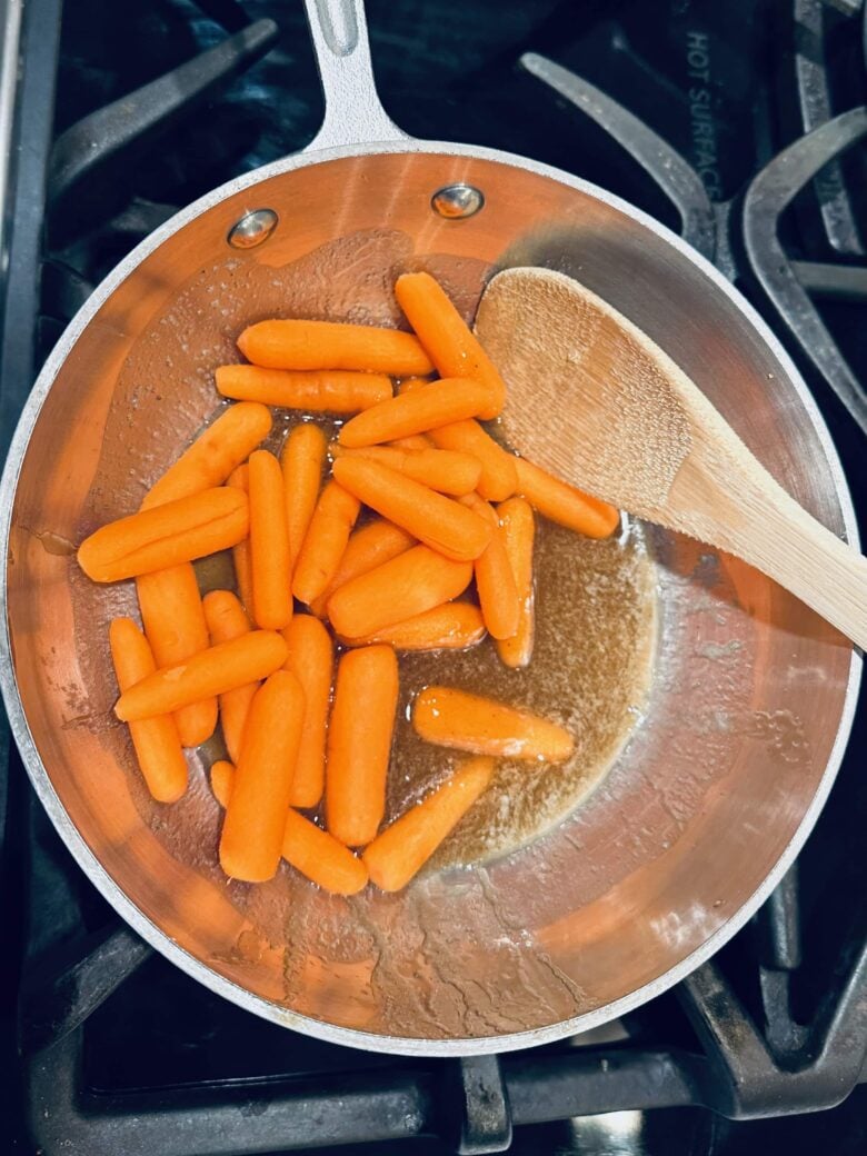 Baby carrots being stirred in a pan with honey glazed carrots ingredients.