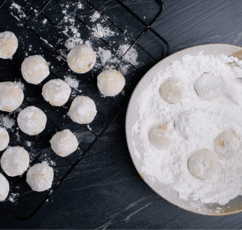 snowball cookies being coated in powdered sugar.