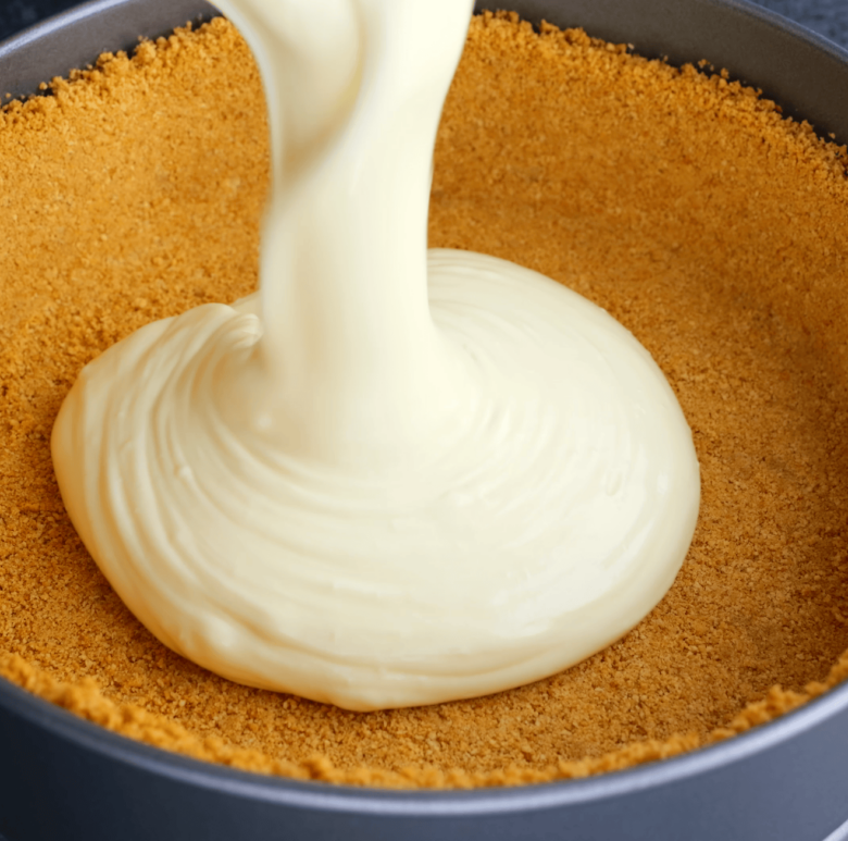 Cheesecake batter being poured into a prepared pan with graham cracker crust.