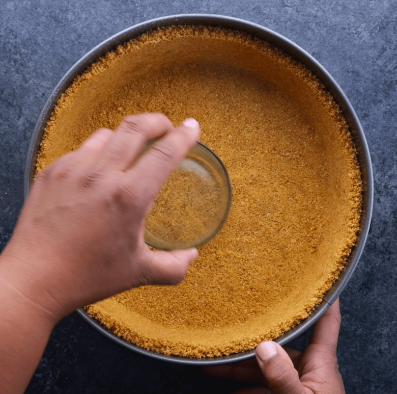 A person pressing down on graham cracker crust with the back of a glass cup.
