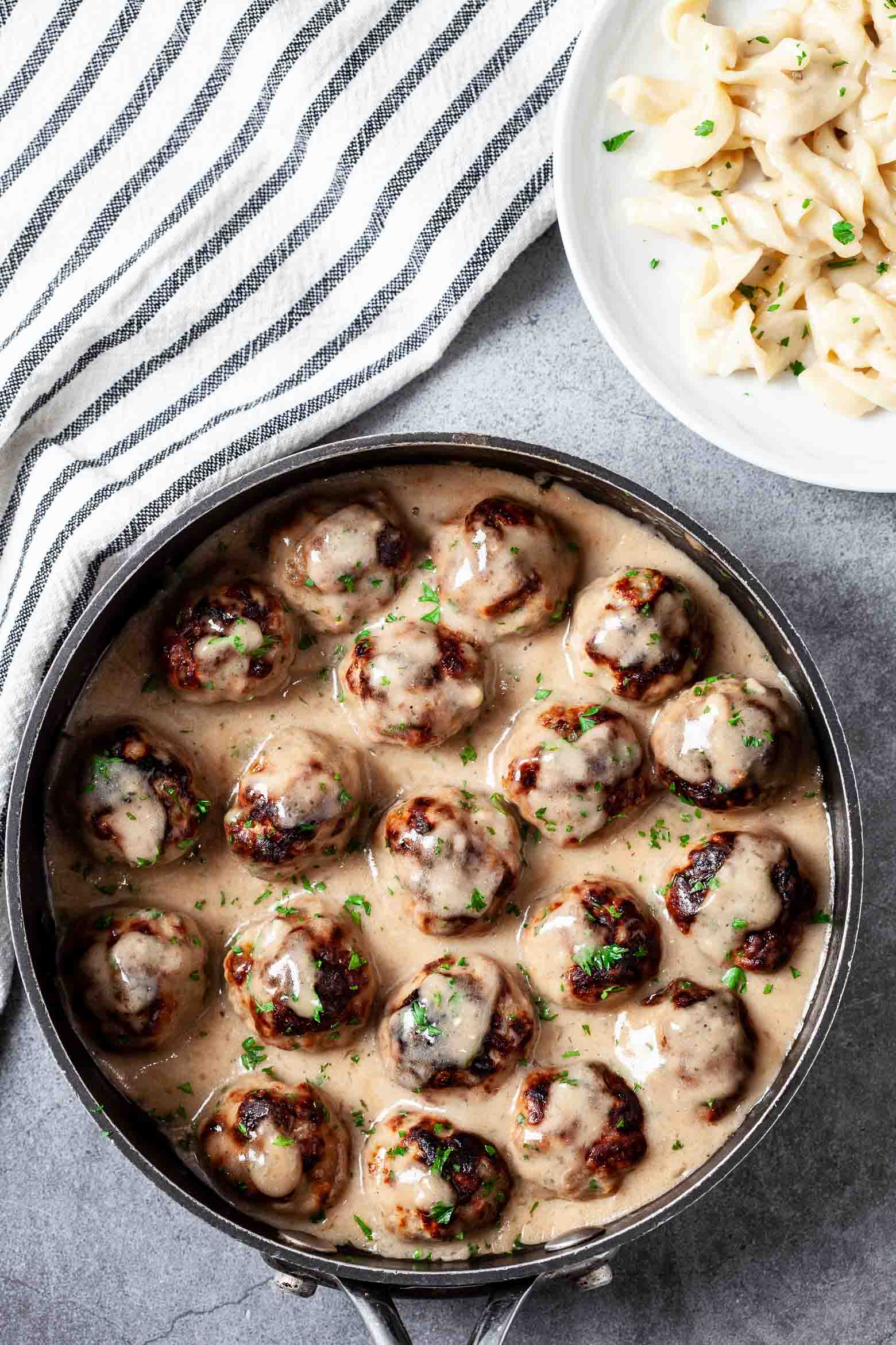 Overhead shot of Swedish meatballs in gravy in a skillet garnished with freshly chopped herbs.