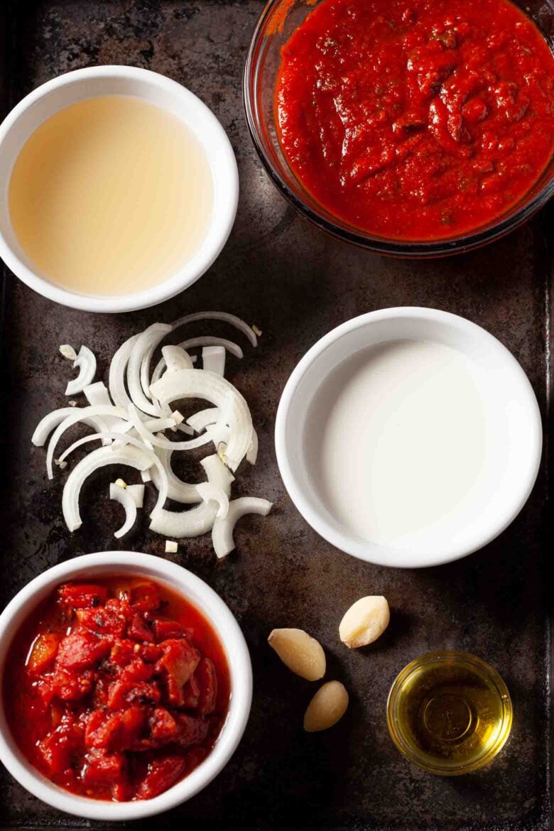 Overhead shot of ingredients for Tuscan tortellini including onions, tomato-based pasta sauce, diced tomatoes, garlic, and olive oil.