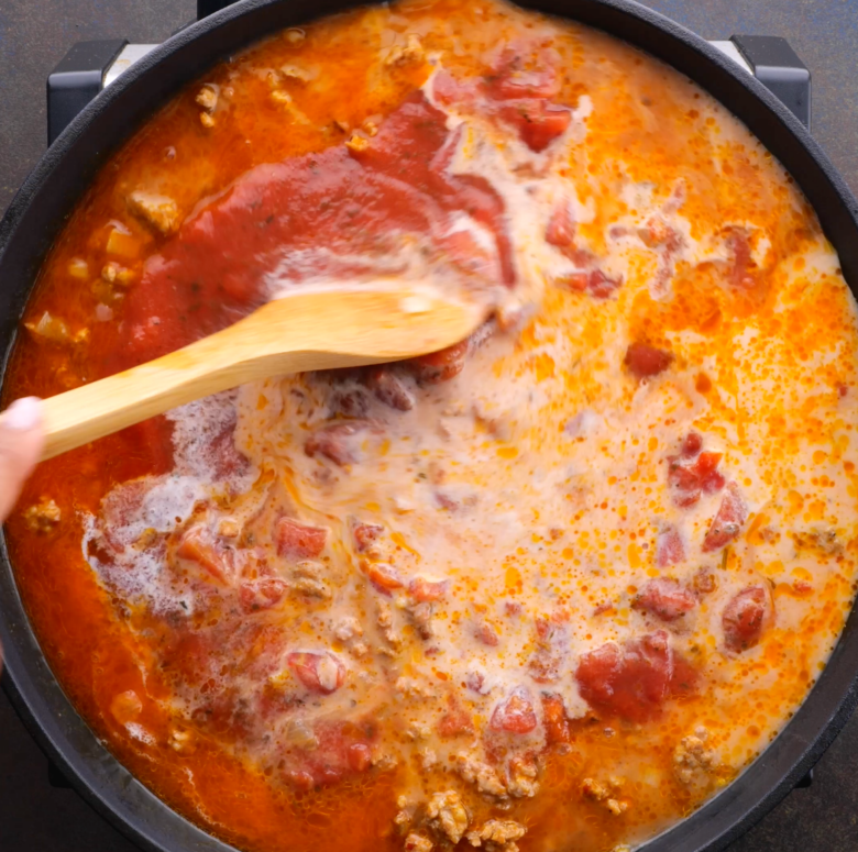 Tomato sauce and diced tomatoes being cooked in a pan with other Tuscan tortellini ingredients.