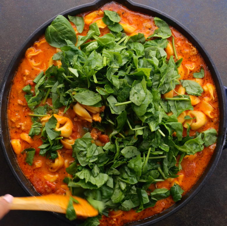 Baby spinach leaves being added to a skillet with Tuscan tortellini.