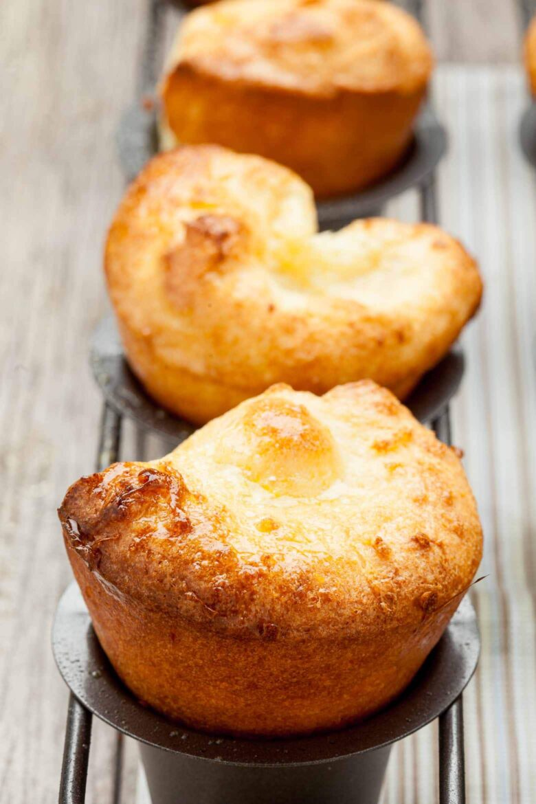 Three popovers in mini popover pans on a wooden table. 