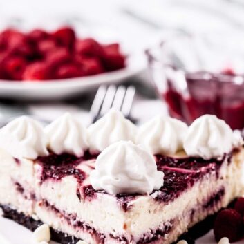 A closeup shot of a slice of raspberry cheesecake on a white plate with whipped cream on top.