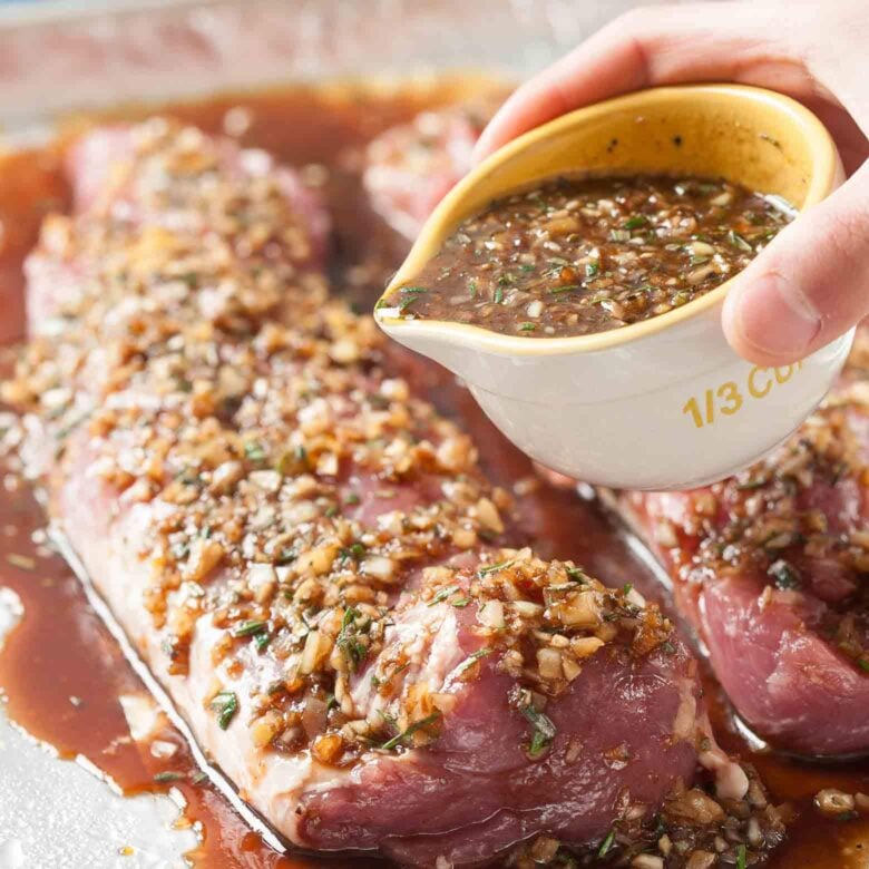 Sheet pan pork tenderloin marinade being poured on top before roasting.