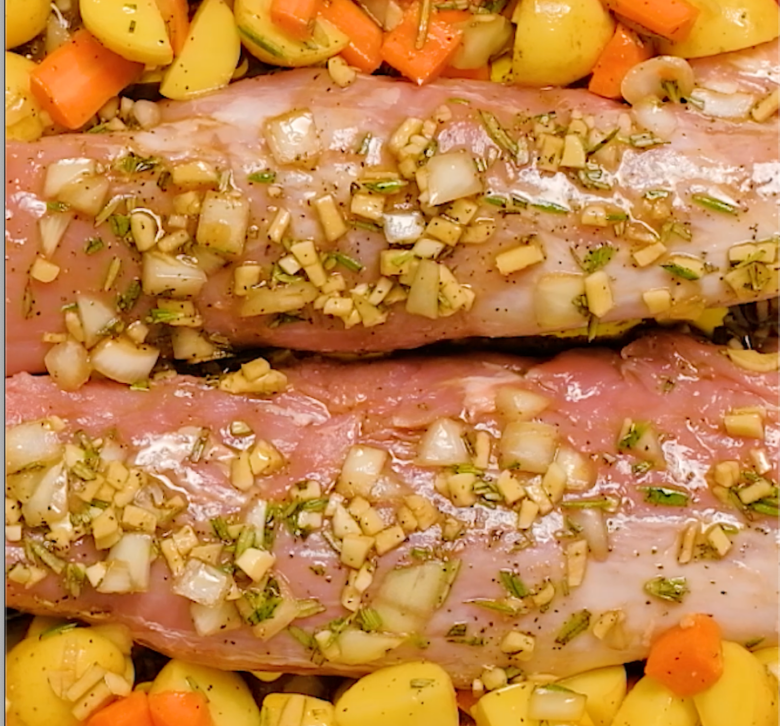 Pork tenderloin with marinade on top and marinated carrots and potatoes around it.