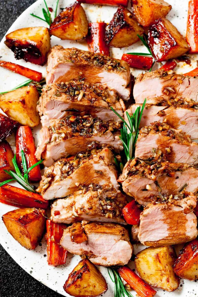 Sheet pan pork tenderloin with roasted carrots and potatoes on a white serving platter.