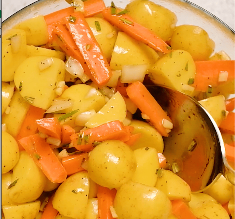 Chopped carrots and potatoes tossed with marinade in a large mixing bowl.