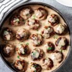 Overhead shot of Swedish meatballs in gravy in a skillet garnished with freshly chopped herbs.