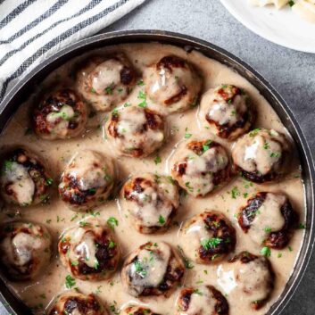 Overhead shot of easy Swedish meatballs recipe in a skillet with buttered noodles on a white plate in the corner.