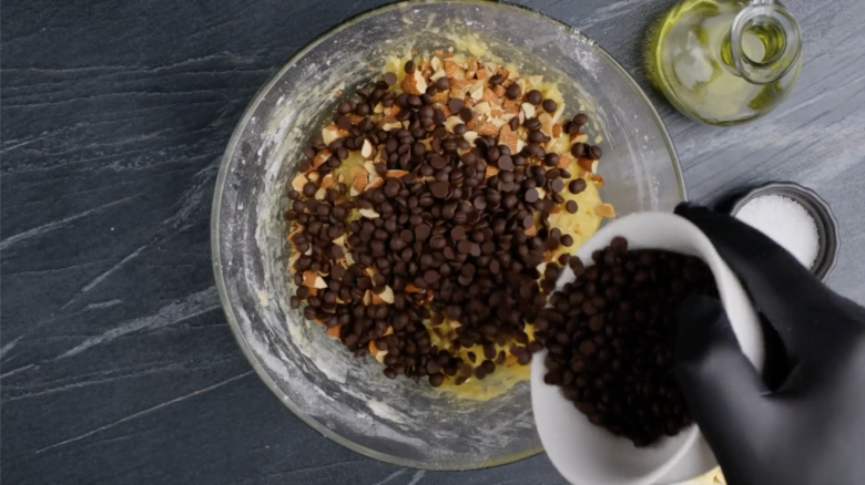 Chocolate chips being added to a mixing bowl to make almond biscotti.