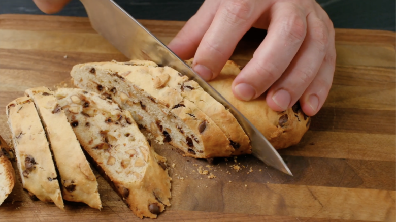 Baked almond biscotti log being sliced with a sharp knife.