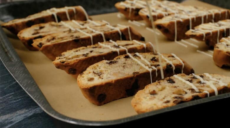 Baked almond biscotti being drizzled with melted white chocolate.