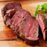 Beef tenderloin with red wine sauce sliced on cutting board.