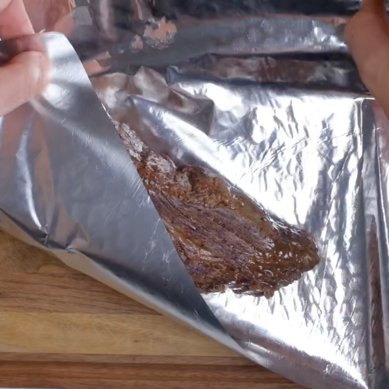 Cooked beef tenderloin being wrapped with aluminum foil.