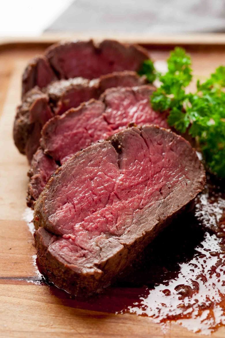 Beef tenderloin roast with red wine sauce sliced on cutting board.