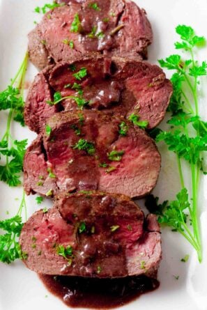 Beef tenderloin slices plated with red wine sauce.