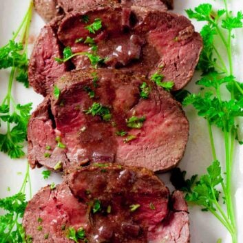 Beef tenderloin slices plated with red wine sauce.