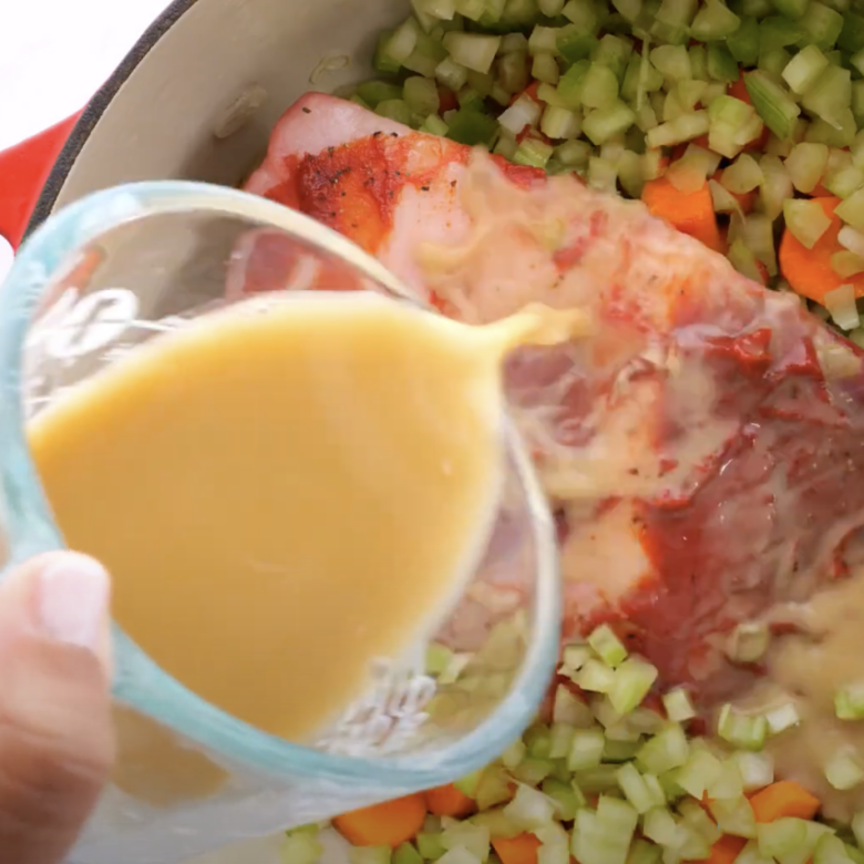 Beef broth mixture being poured over beef brisket in a Dutch oven.