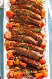 Sliced tender braised beef on a serving plate with carrots and garnished with fresh parsley.