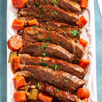 Sliced tender braised beef on a serving plate with carrots and garnished with fresh parsley.