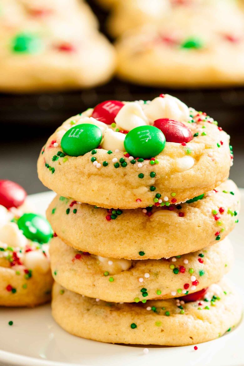 Close up shot of stacked M&M Christmas Cookies with red and green M&Ms, sprinkles, and white chocolate chips on top. 