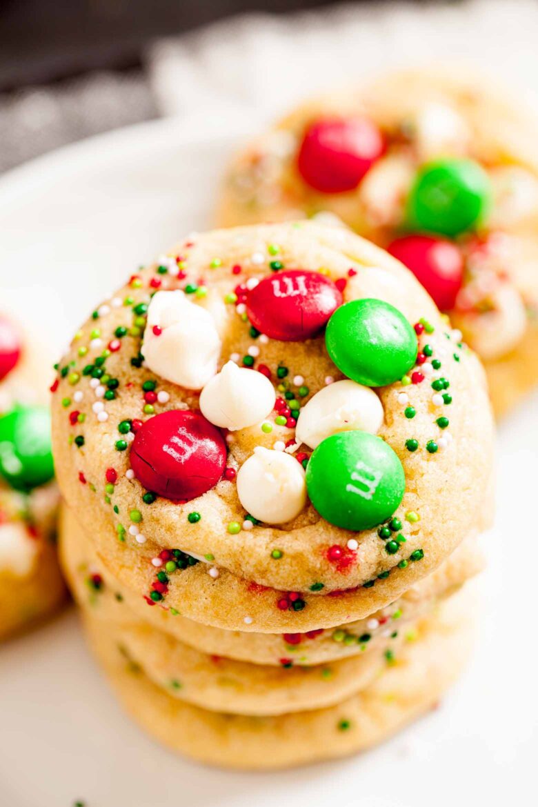 Close up shot of stacked M&M Christmas Cookies with red and green M&Ms, sprinkles, and white chocolate chips on top.