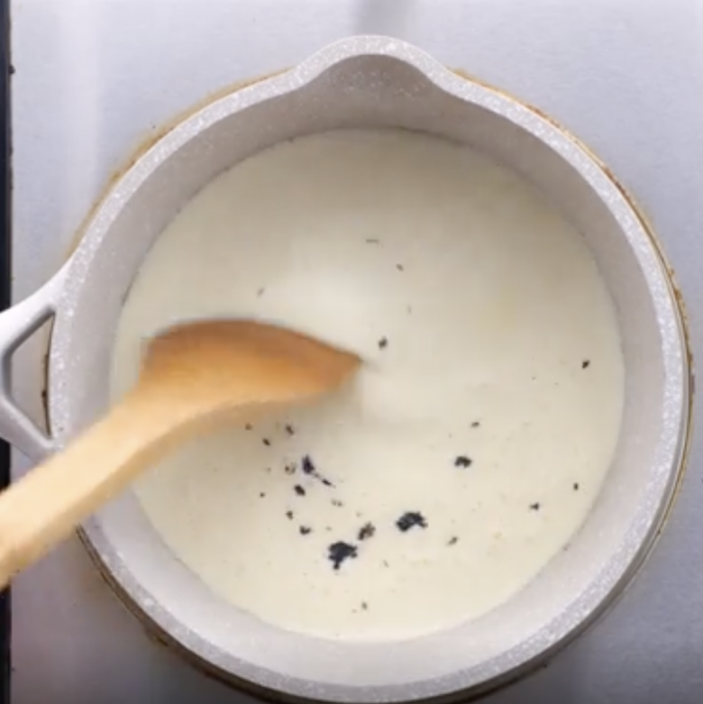 A saucepan with cream mixture with visible vanilla bean seeds.
