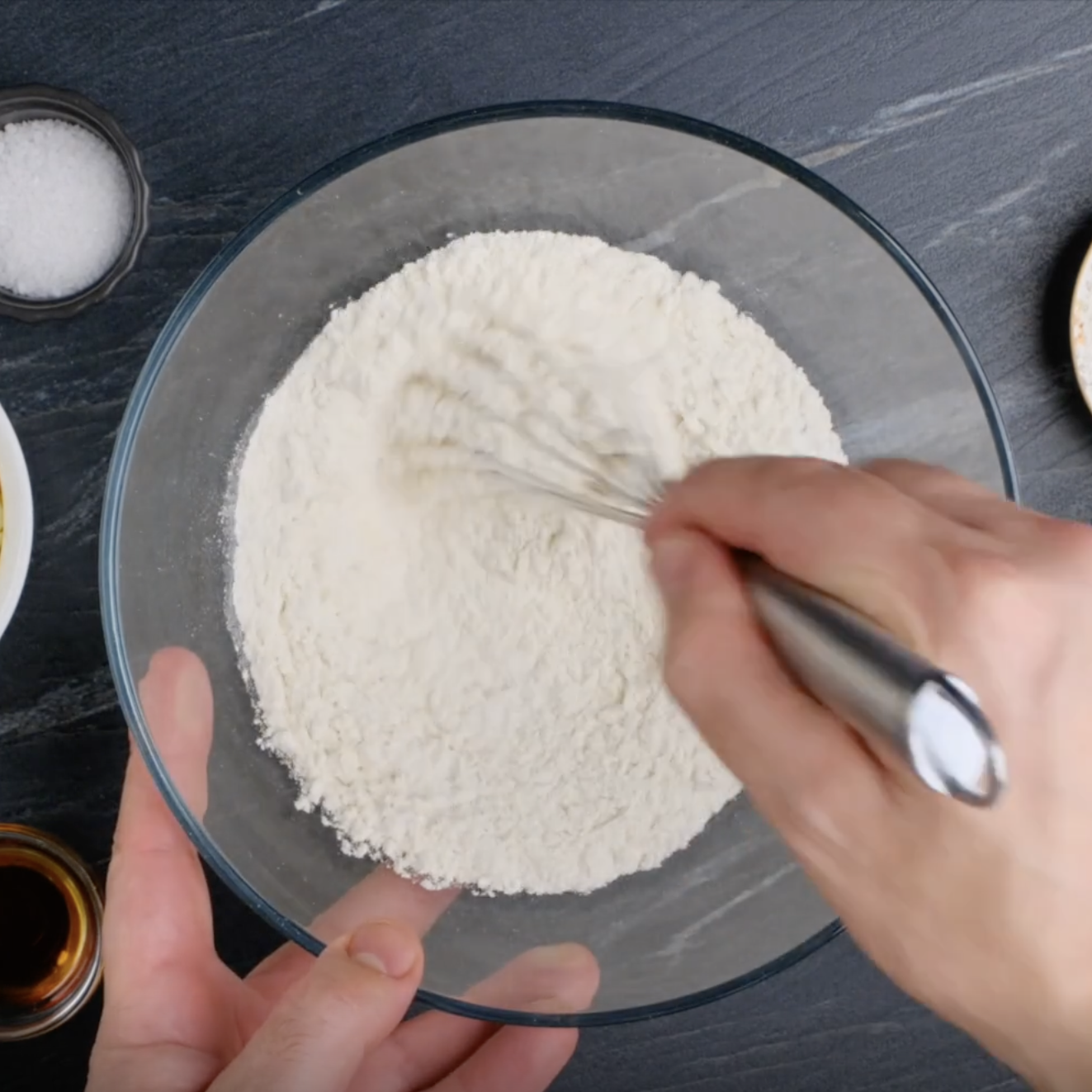 A flour mixture being whisked by hand in a glass mixing bowl.