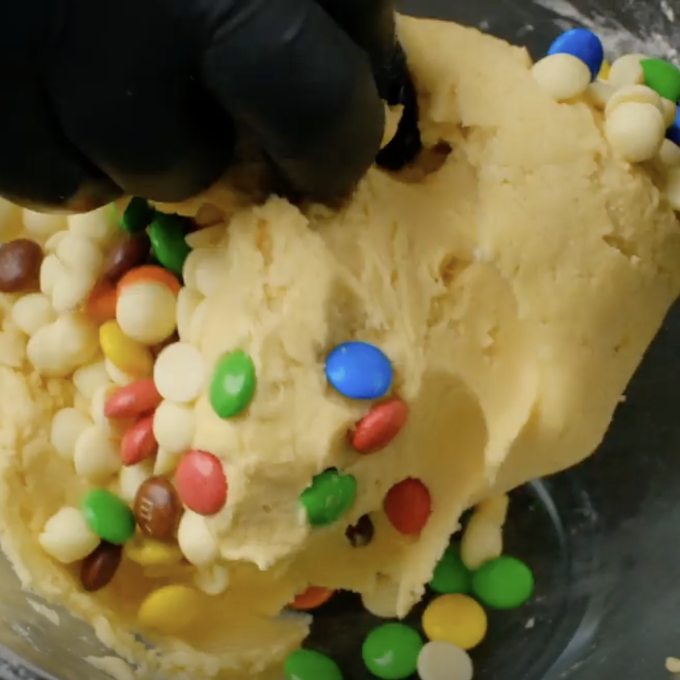 M&Ms being mixed into cookie dough by hand.