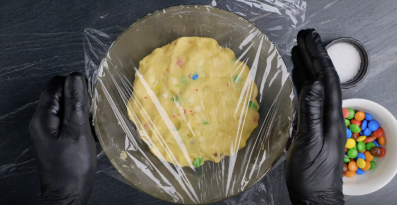 A bowl with M&M cookie dough covered with plastic wrap.