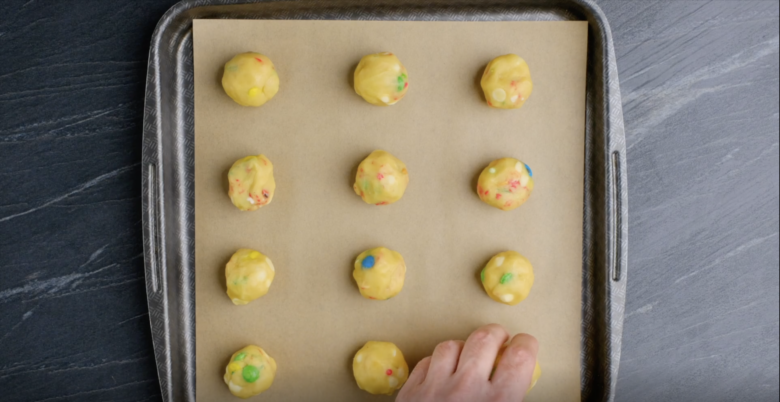 1-inch M&M cookie dough balls on a baking sheet lined with parchment paper.