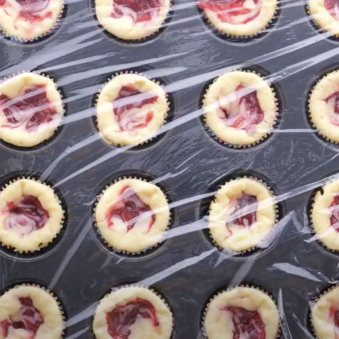 Baked mini cheesecakes covered with plastic wrap.