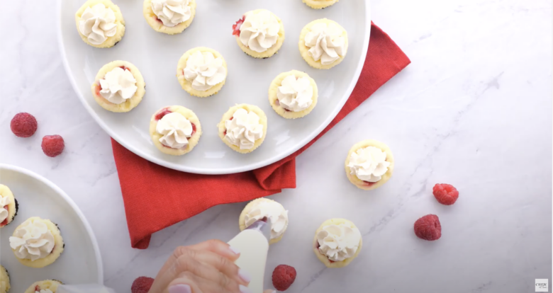 Stabilized whipped cream being piped onto mini cheesecakes.