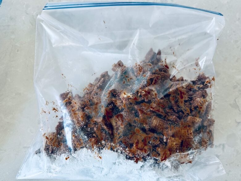 A plastic bag with powdered sugar and chocolate coated Chex cereal.