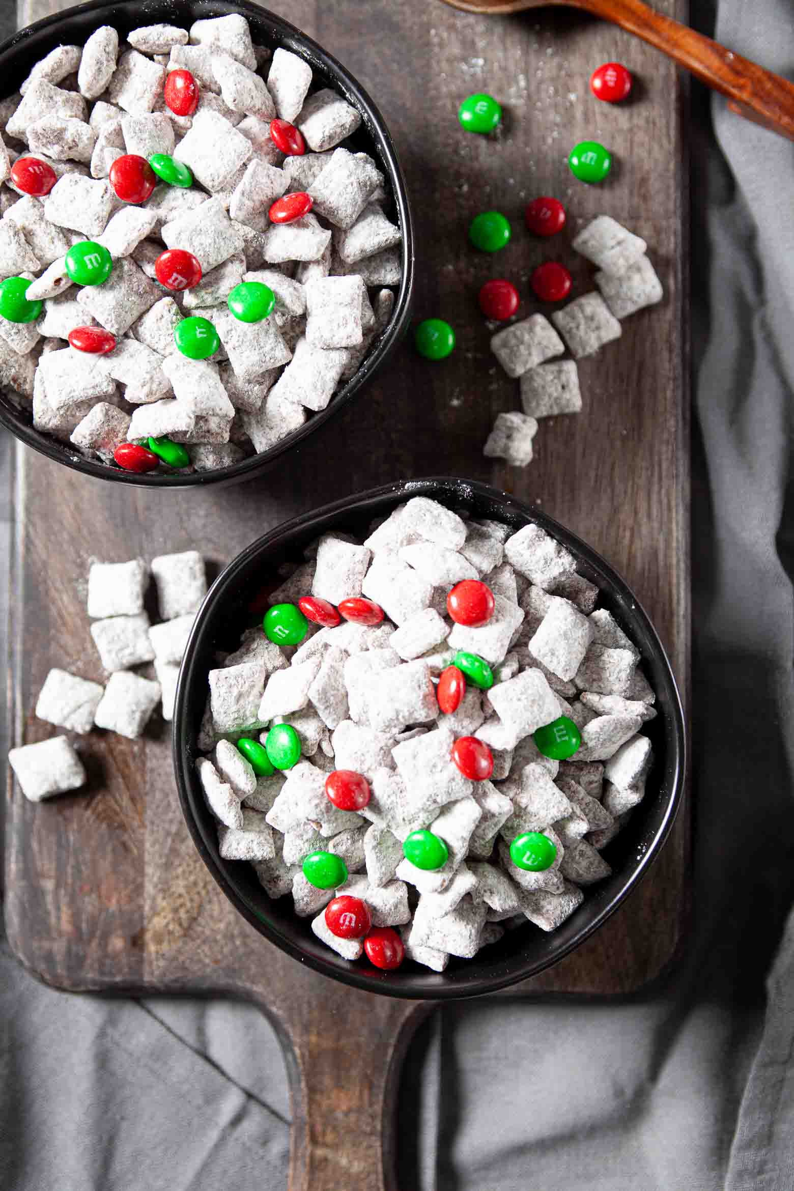 Overhead shot of two bowls of Muddy Buddies topped with red and green M&Ms.
