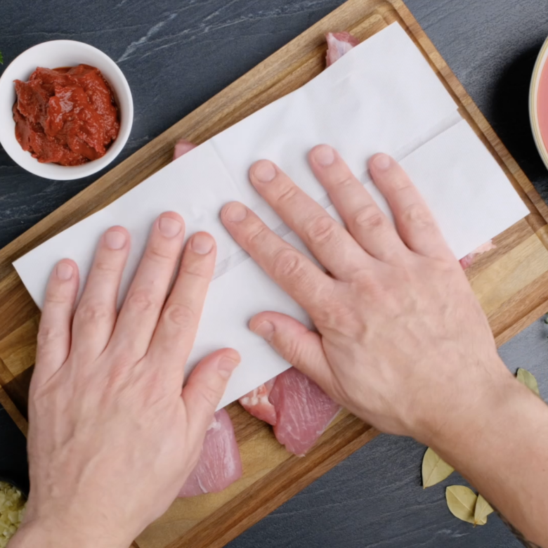 A person towel-drying pork to make pork ragu.