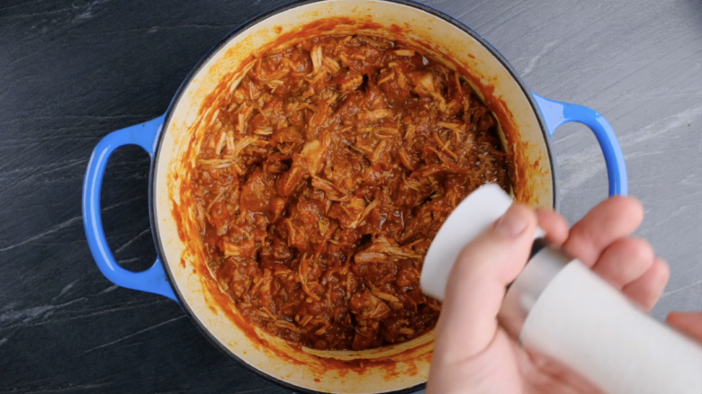 Cooked shredded pork being seasoned with salt in a Dutch oven.