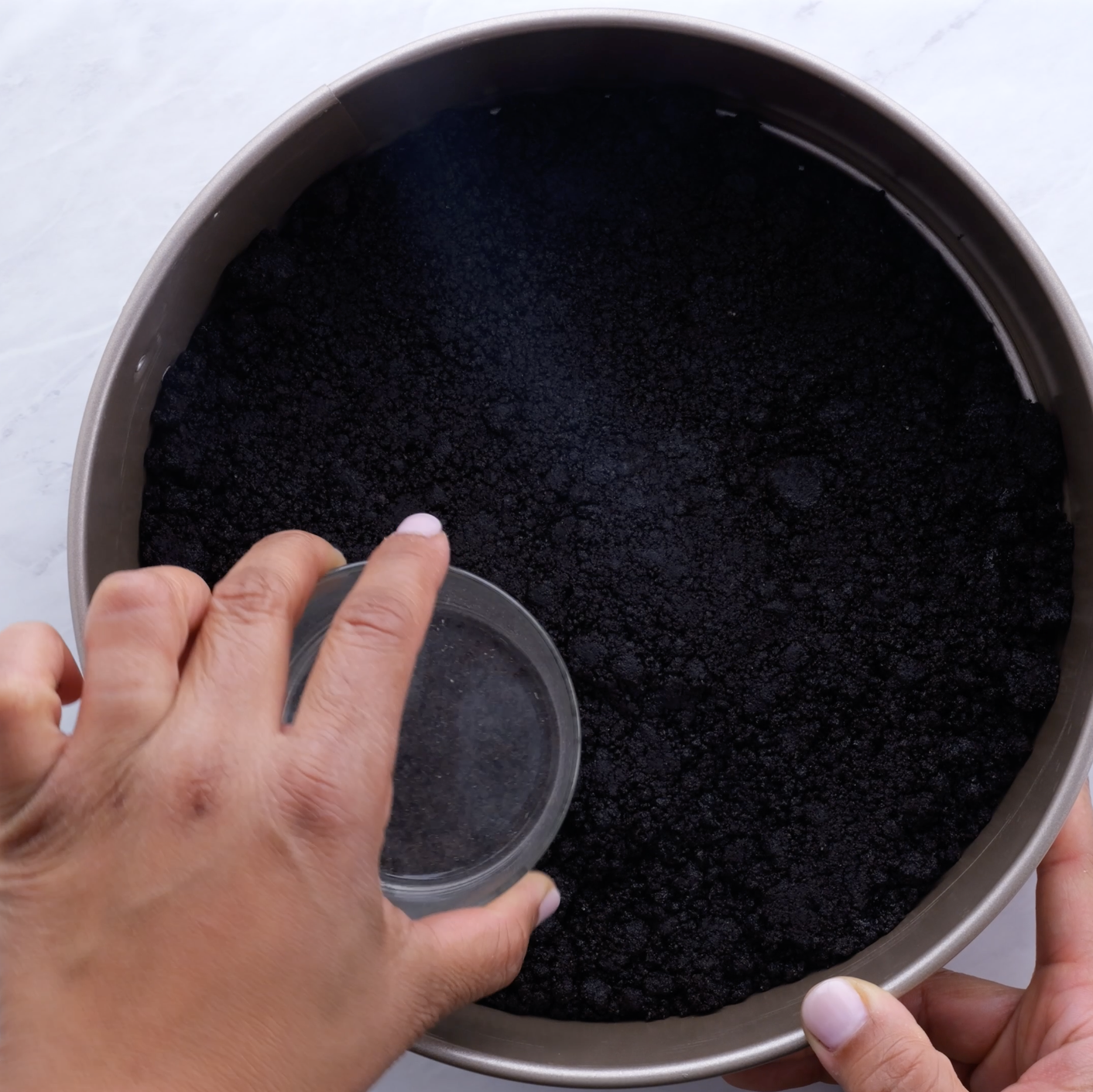 A person pressing down on chocolate cookie crust with the back of a glass cup.