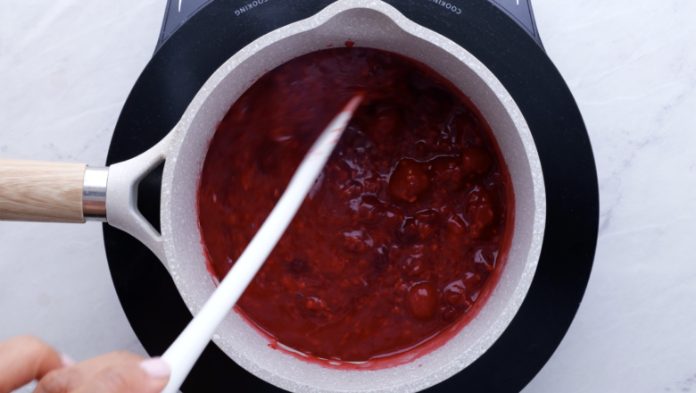 Raspberry sauce mixture being cooked in a white saucepan.