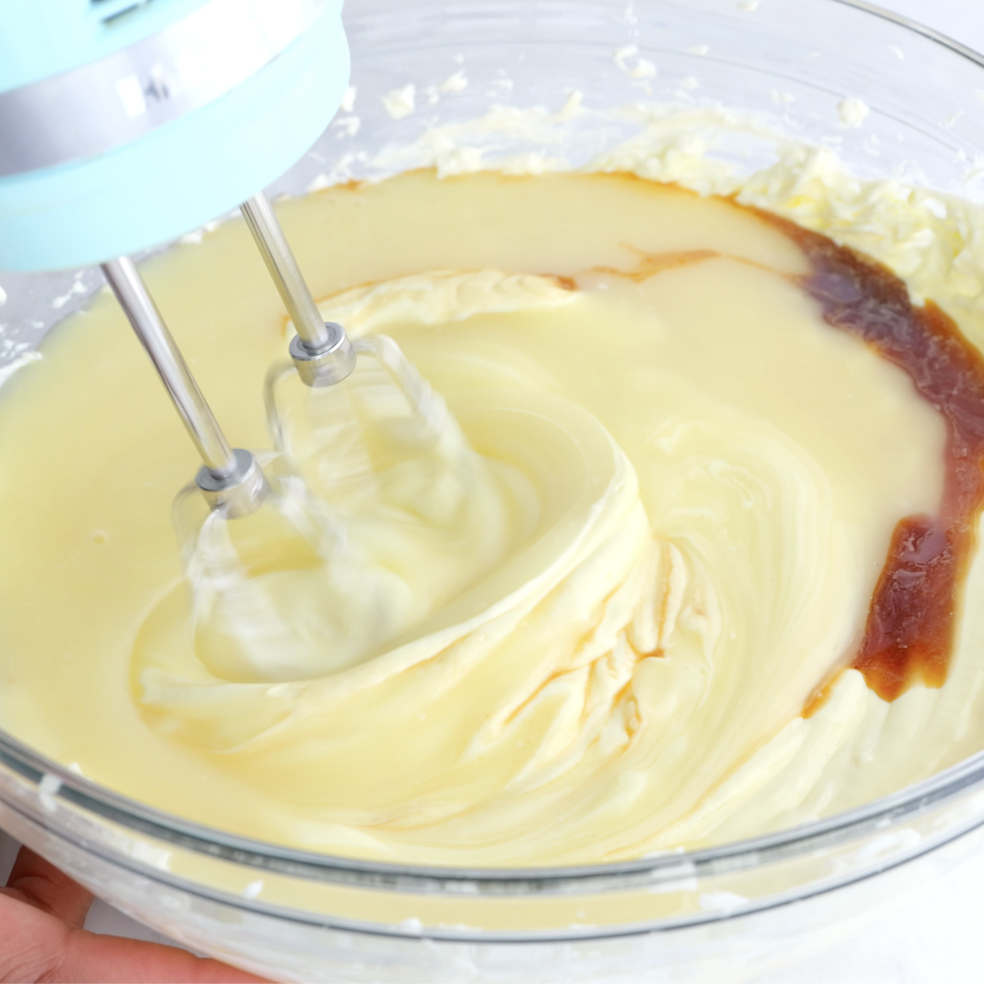 Cheesecake mixture being mixed in a glass bowl with a hand mixer. 