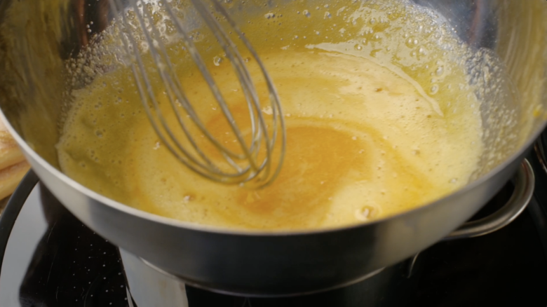 Egg yolks, marsala, and sugar being whisked on top of a saucepan of simmering water.