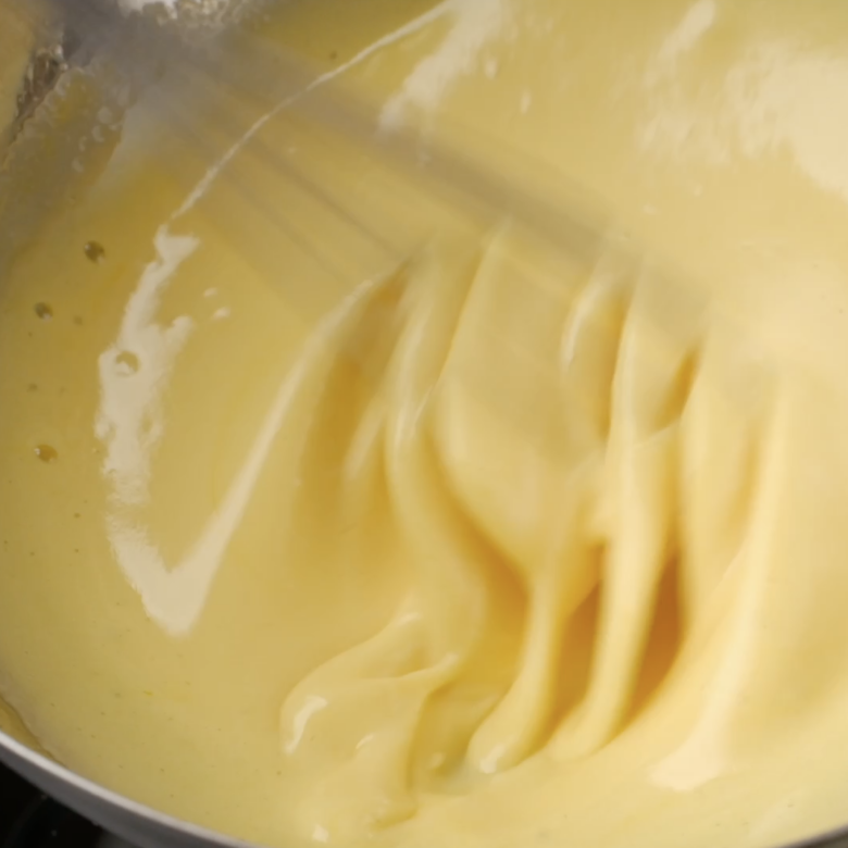 An egg yolk mixture being whisked in a metal bowl.