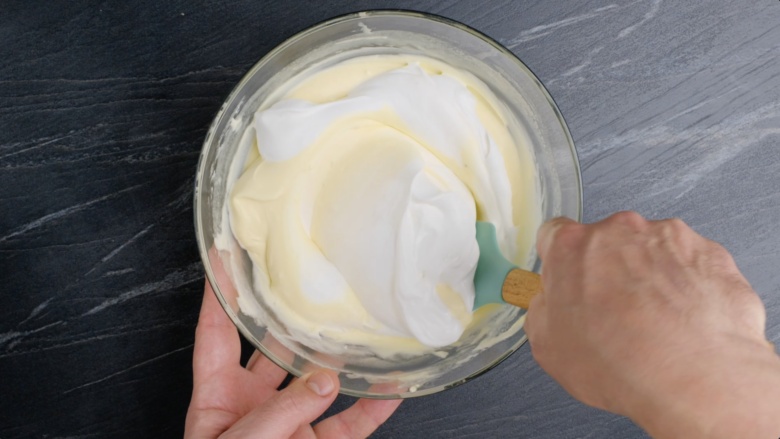 Whipped heavy cream being folded into mascarpone mixture to make tiramisu cake.